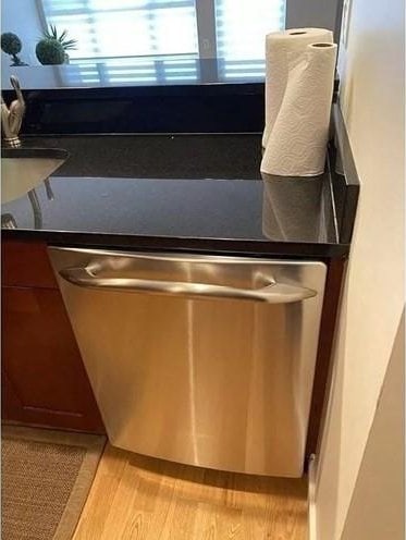 detailed view of stainless steel dishwasher, light wood-style floors, and dark countertops