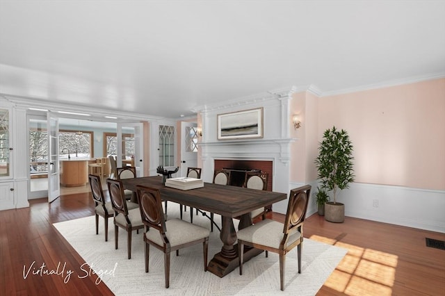 dining area featuring ornamental molding, a fireplace, wood finished floors, and visible vents