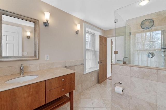 full bath with vanity, tile walls, wainscoting, a shower stall, and tile patterned floors