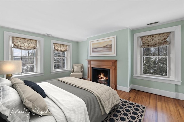 bedroom featuring a warm lit fireplace, wood finished floors, visible vents, and baseboards