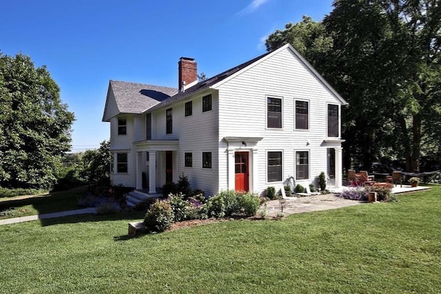 back of property with a chimney, a lawn, and a patio area