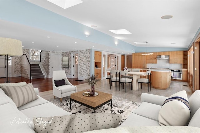 living room with light wood-style flooring, recessed lighting, stairs, lofted ceiling with skylight, and wallpapered walls