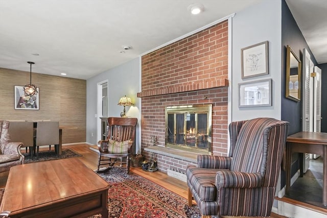 living area featuring baseboards, an accent wall, recessed lighting, a brick fireplace, and wood finished floors