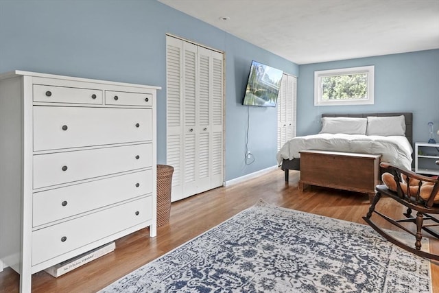 bedroom featuring baseboards, wood finished floors, and two closets