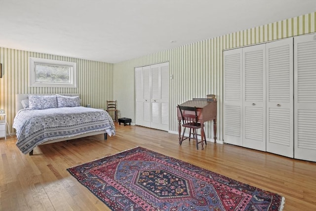 bedroom with wallpapered walls, wood finished floors, and multiple closets
