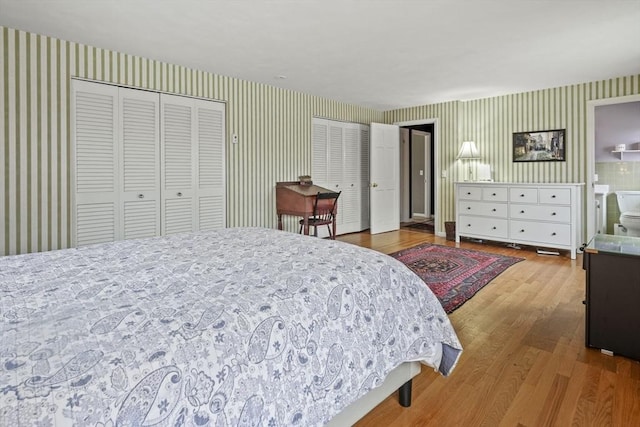 bedroom featuring wallpapered walls, multiple closets, and wood finished floors