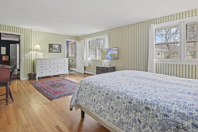 bedroom with a baseboard heating unit, wallpapered walls, and wood finished floors
