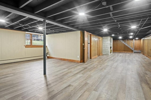 below grade area featuring a baseboard radiator, wooden walls, wood finished floors, and stairs