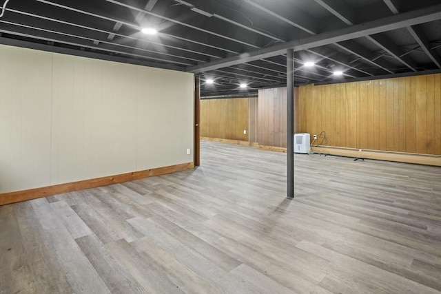 finished basement with a baseboard radiator, baseboards, wood walls, and wood finished floors