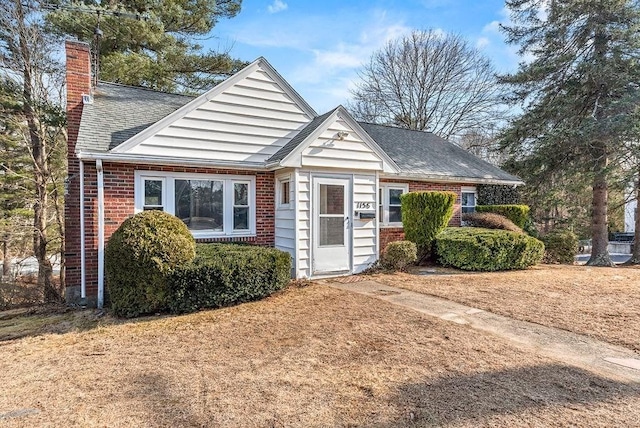 bungalow featuring a shingled roof, brick siding, and a chimney