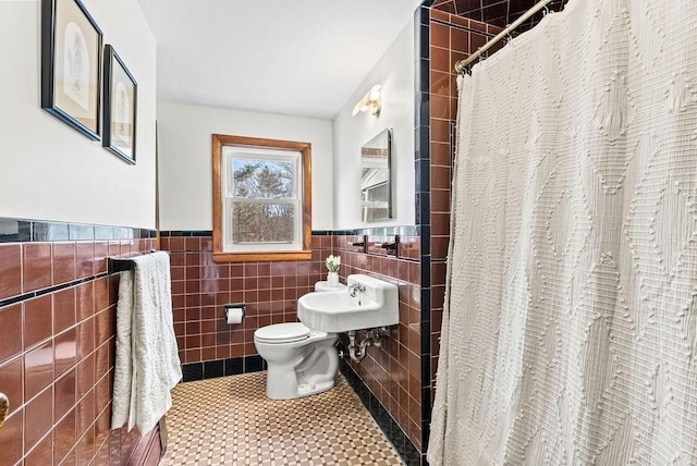 bathroom with toilet, curtained shower, tile walls, and a wainscoted wall