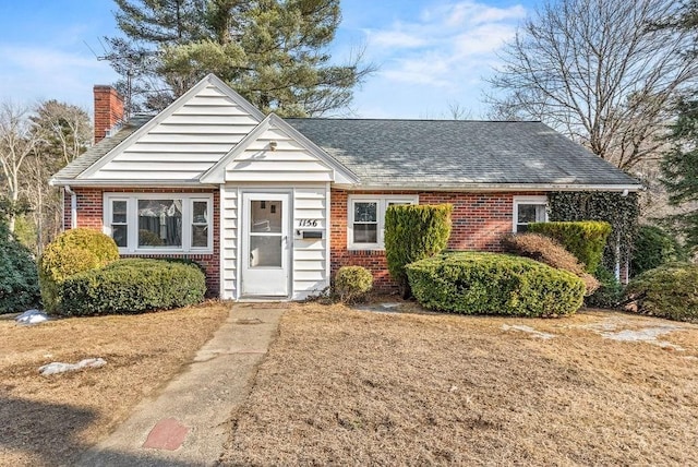 view of front of house featuring roof with shingles, a chimney, and brick siding