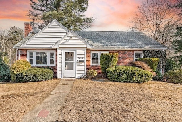 view of front of home featuring roof with shingles, a chimney, a lawn, and brick siding