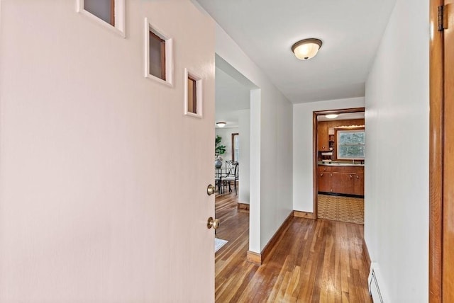 corridor featuring baseboards, baseboard heating, and wood finished floors