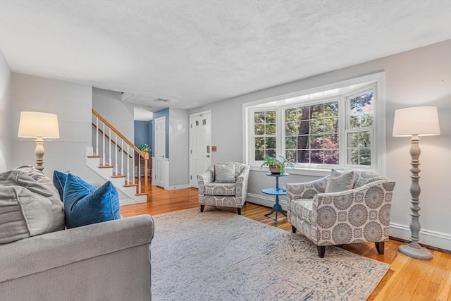 16 Vanderbelt Rd, Acton, MA 01720 - living area with baseboard heating, wood finished floors, stairway, baseboards, and a textured ceiling