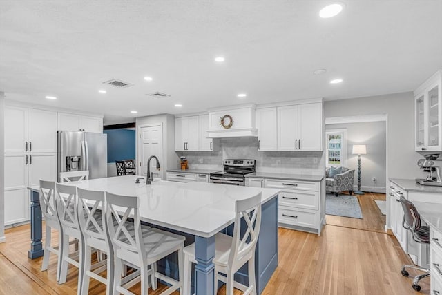 16 Vanderbelt Rd, Acton, MA 01720 - kitchen featuring appliances with stainless steel finishes, light wood-style flooring, white cabinets, backsplash, and a center island with sink