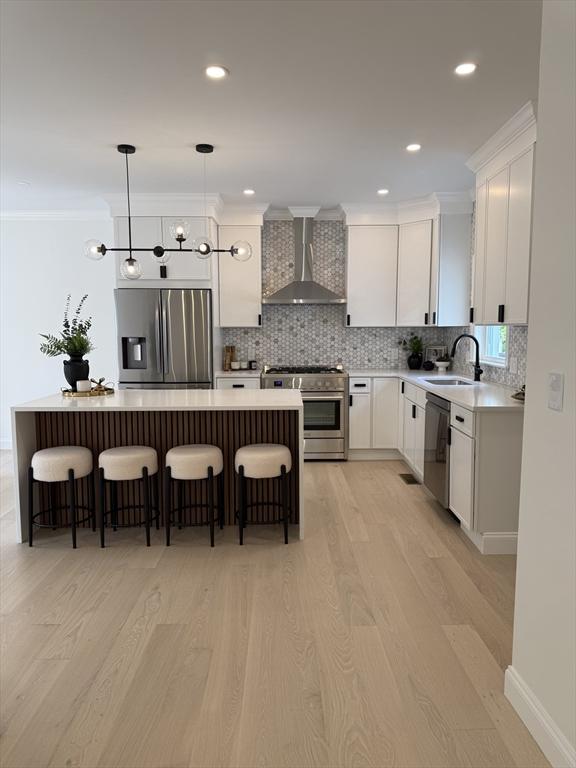 kitchen featuring appliances with stainless steel finishes, wall chimney exhaust hood, light wood-style flooring, ornamental molding, and recessed lighting