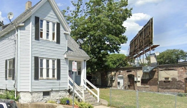 view of front facade with entry steps, a front lawn, a shingled roof, and fence