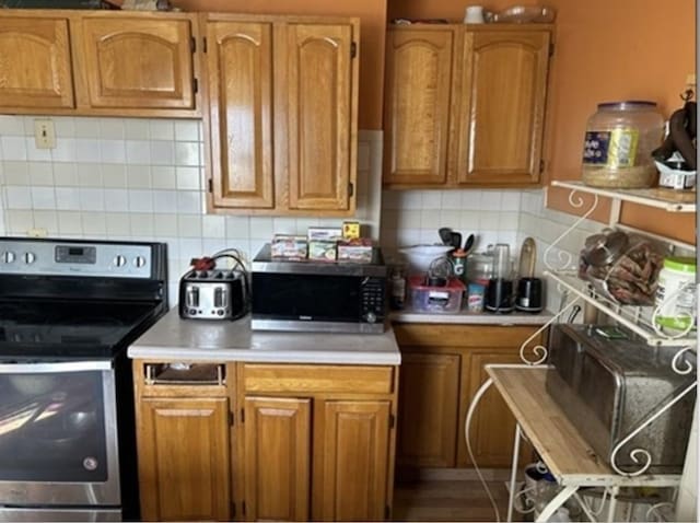 kitchen with stainless steel appliances, brown cabinetry, light countertops, and decorative backsplash