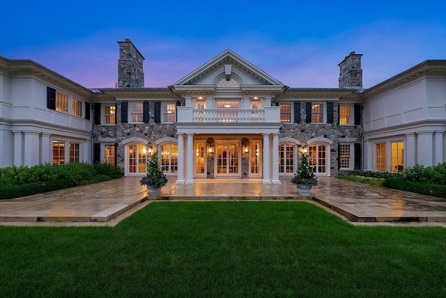 180 Ash St, Weston, MA 02493 - back of property at dusk featuring a balcony, stone siding, a chimney, and a lawn