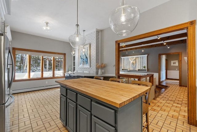 kitchen with brick floor, a breakfast bar, gray cabinets, baseboard heating, and butcher block countertops