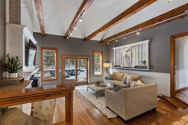 living area featuring lofted ceiling with beams, a wainscoted wall, hardwood / wood-style flooring, a decorative wall, and track lighting