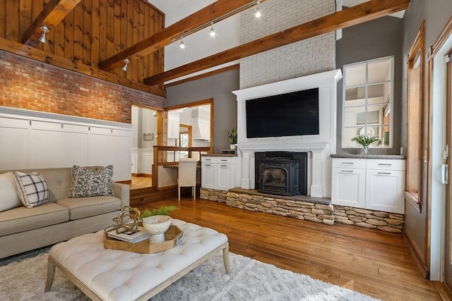 living area with wainscoting, hardwood / wood-style flooring, brick wall, beam ceiling, and track lighting