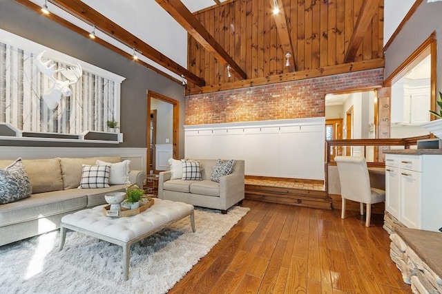 living room with brick wall, a wainscoted wall, beamed ceiling, and hardwood / wood-style floors