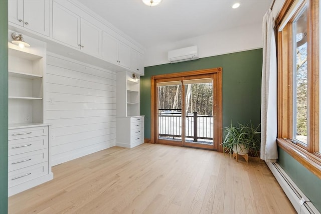 interior space with a baseboard heating unit, light wood-type flooring, an AC wall unit, and a healthy amount of sunlight