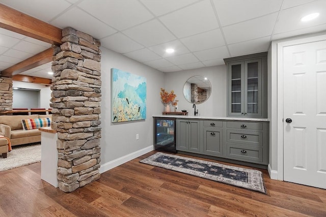 bar with a paneled ceiling, bar, beverage cooler, wood finished floors, and baseboards