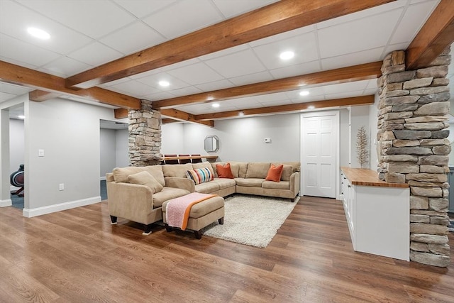 living area featuring ornate columns, baseboards, dark wood-style floors, and a drop ceiling