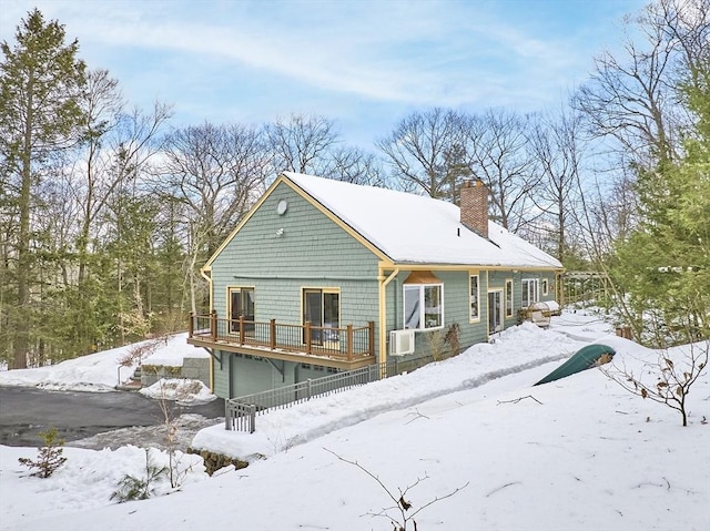 snow covered back of property with a garage, a chimney, a deck, and cooling unit