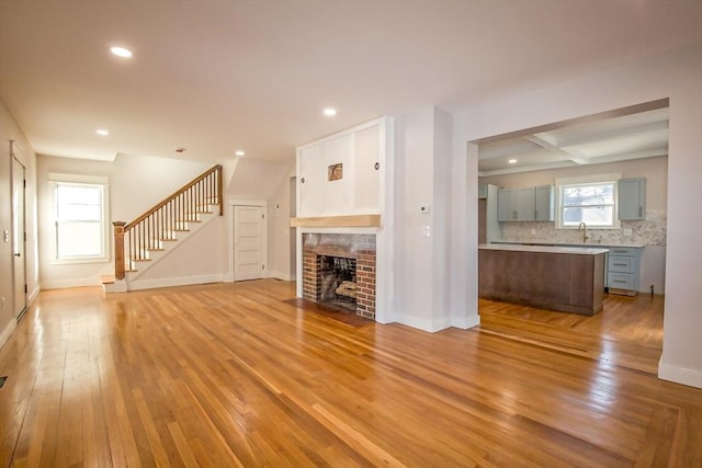 unfurnished living room with a brick fireplace, coffered ceiling, sink, beam ceiling, and light hardwood / wood-style flooring