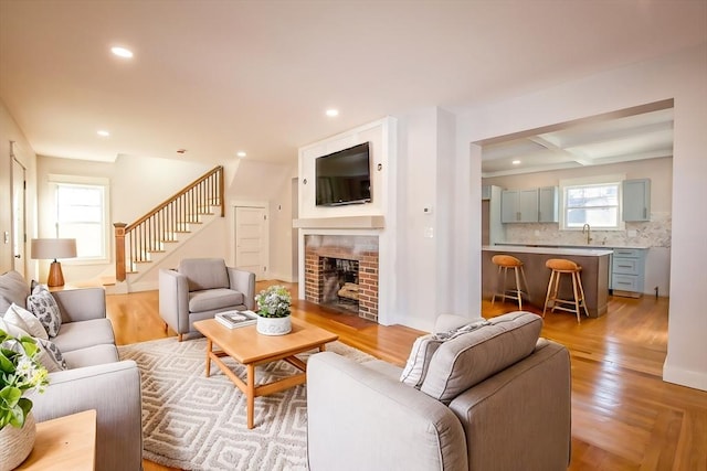 living room with sink, beamed ceiling, light hardwood / wood-style flooring, and a brick fireplace