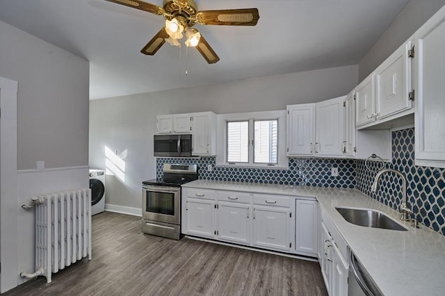 kitchen with washer / dryer, sink, white cabinetry, appliances with stainless steel finishes, and radiator