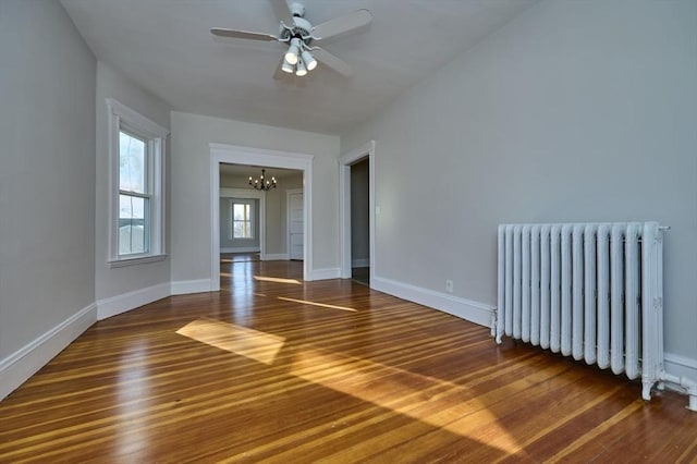 unfurnished room featuring hardwood / wood-style flooring, radiator heating unit, and ceiling fan with notable chandelier