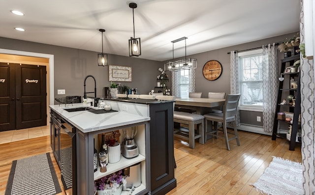 kitchen with pendant lighting, a kitchen island with sink, sink, light hardwood / wood-style flooring, and light stone counters