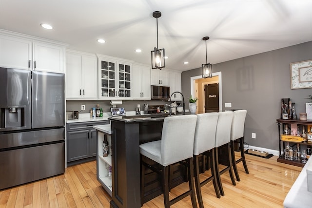 kitchen with white cabinets, decorative light fixtures, light hardwood / wood-style floors, and stainless steel appliances