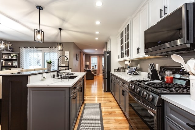 kitchen featuring pendant lighting, white cabinets, a center island with sink, appliances with stainless steel finishes, and light hardwood / wood-style floors