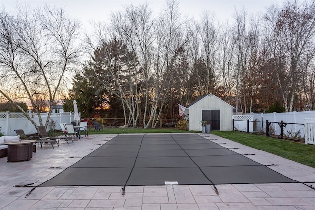 pool at dusk with a lawn, a patio area, and a shed