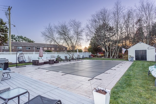 pool at dusk featuring outdoor lounge area, a patio, an outdoor structure, and a lawn