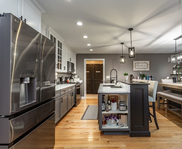 kitchen featuring stainless steel appliances, pendant lighting, light hardwood / wood-style flooring, white cabinets, and an island with sink