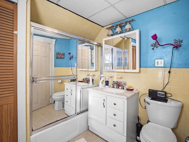 full bathroom featuring tile patterned flooring, a paneled ceiling, toilet, enclosed tub / shower combo, and vanity