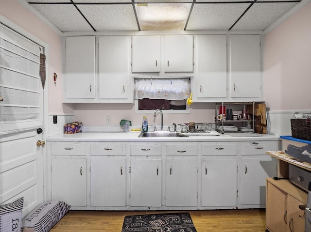 kitchen featuring a paneled ceiling, white cabinetry, sink, and light wood-type flooring