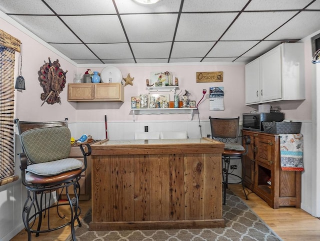 bar featuring white cabinets, a paneled ceiling, and light wood-type flooring