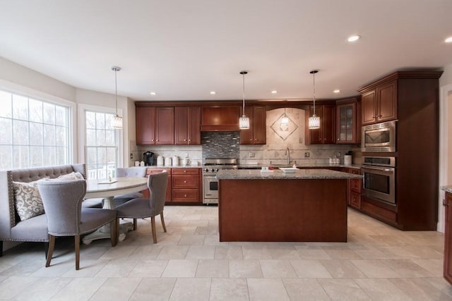 kitchen with appliances with stainless steel finishes, stone countertops, decorative light fixtures, decorative backsplash, and a center island with sink