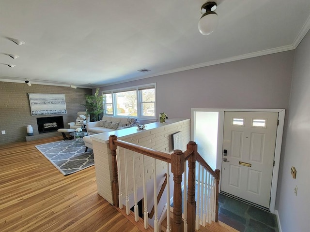 foyer with crown molding, brick wall, a fireplace, and hardwood / wood-style floors