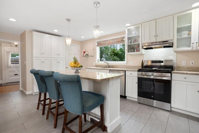 518 Washington St, Winchester, MA 01890 - kitchen with stainless steel appliances, under cabinet range hood, a breakfast bar, white cabinetry, and a kitchen island