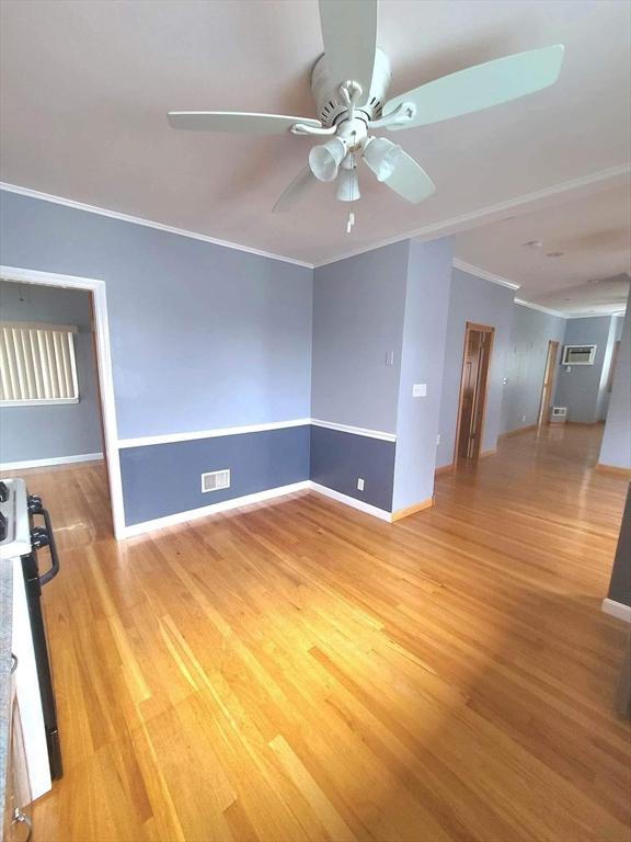 empty room with light wood finished floors, visible vents, baseboards, a ceiling fan, and crown molding