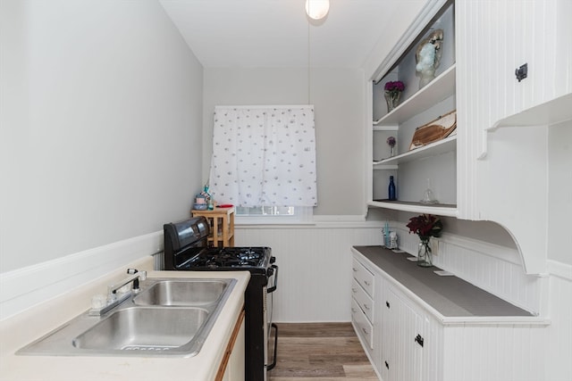 kitchen with hardwood / wood-style flooring, white cabinetry, black gas stove, and sink